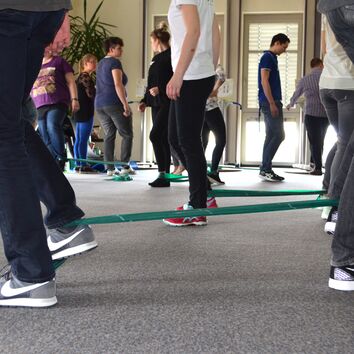 Gruppe arbeitet Paarweise mit Therabändern an den Füßen